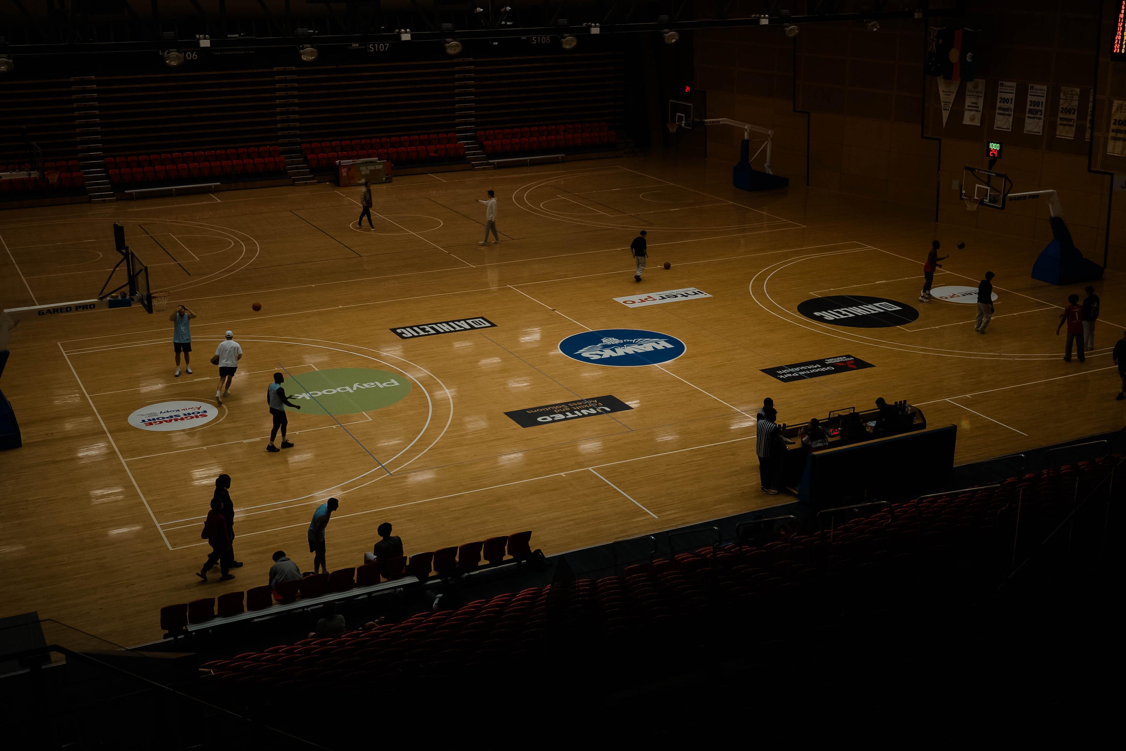 Players warming up on court in a large arena with empty tiered seating.
