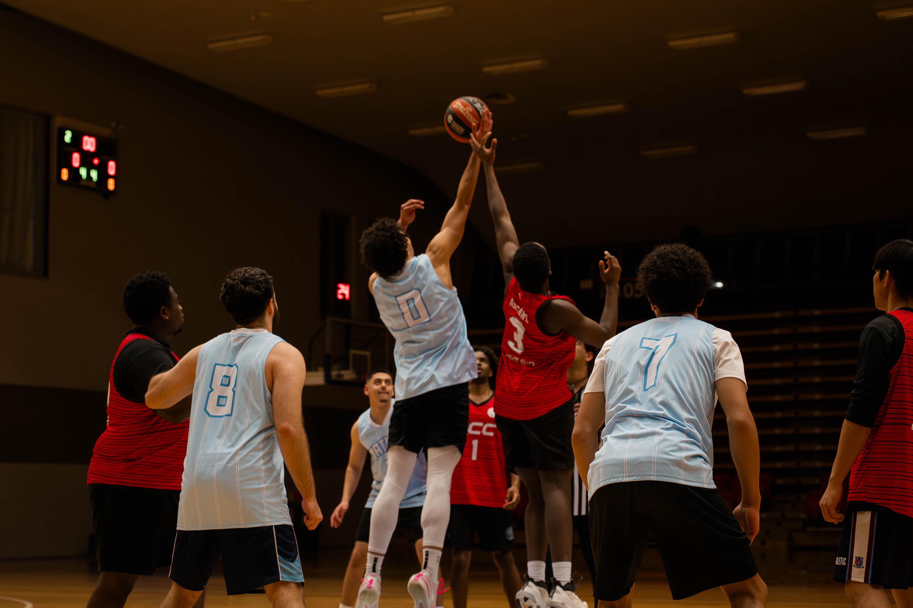 Two players leap to contest the tip-off at centre court during a CBL game.