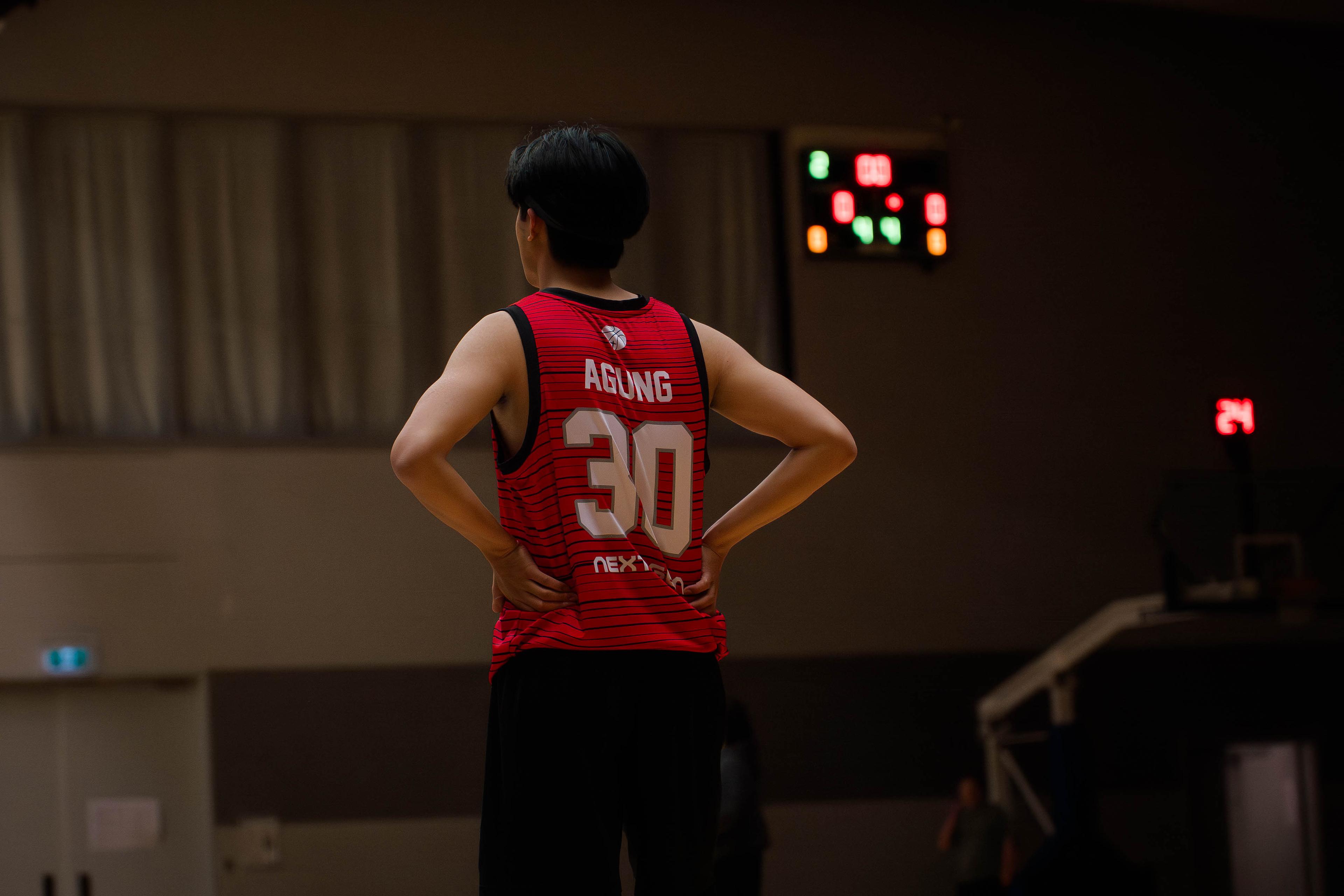 Player in a red number 30 jersey stands hands on hips watching the game clock.