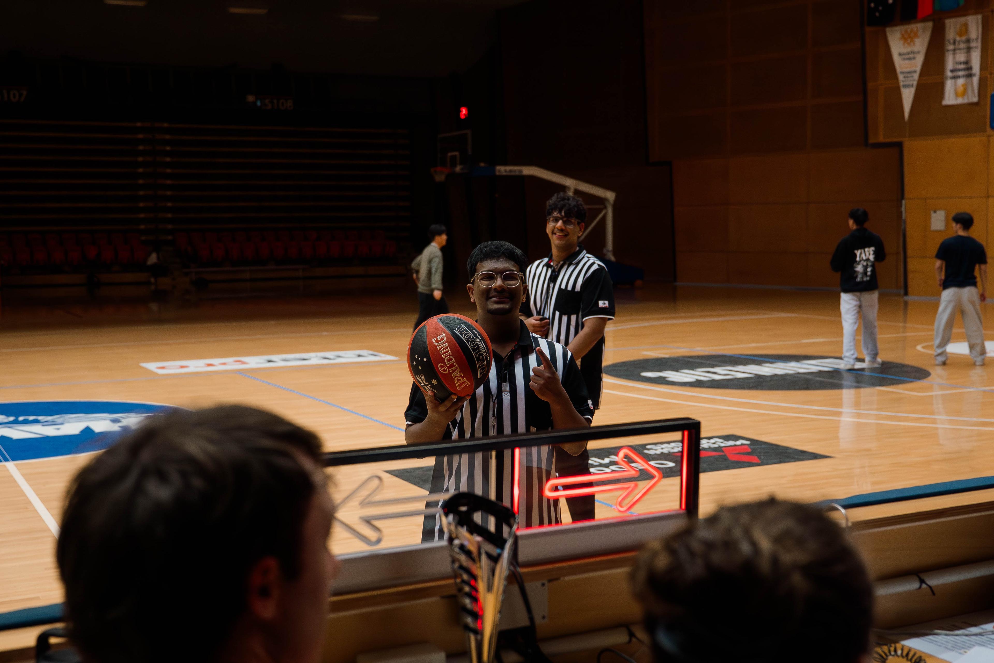 Referee smiling and holding a basketball on court before a game.