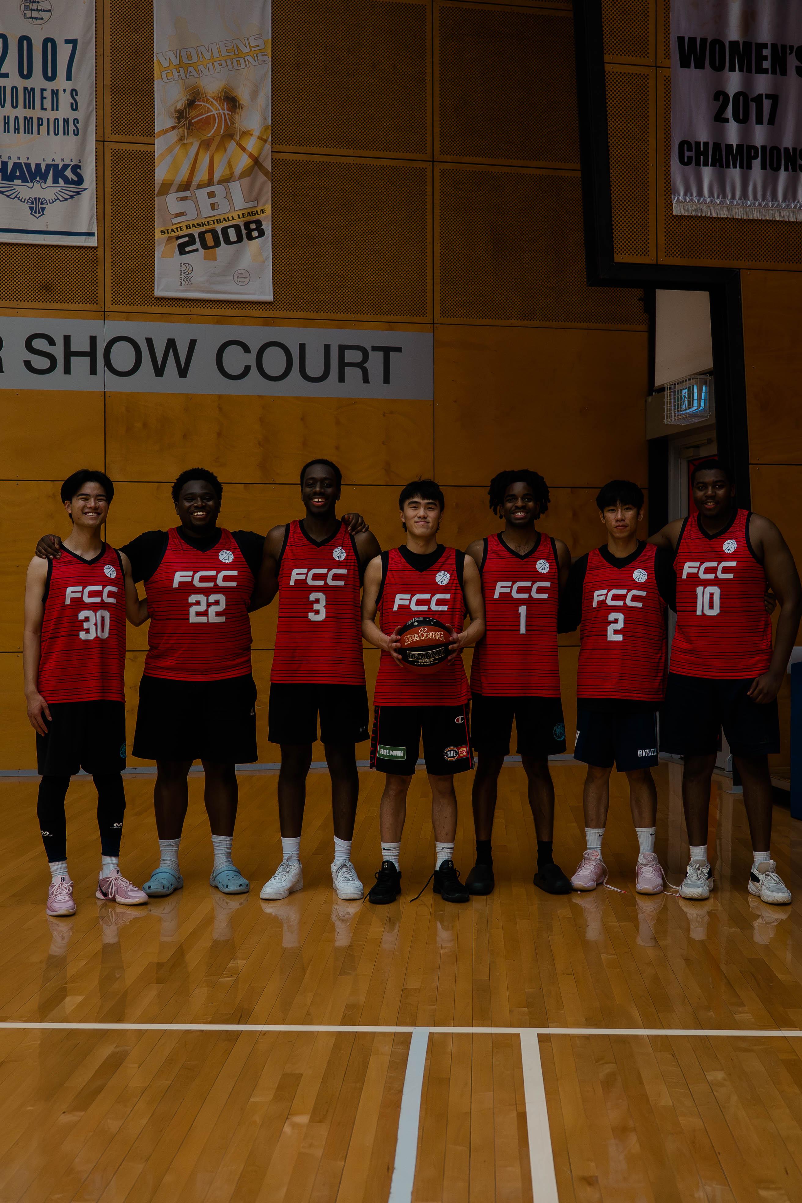 Team in red jerseys posing in a row on court beneath championship banners.